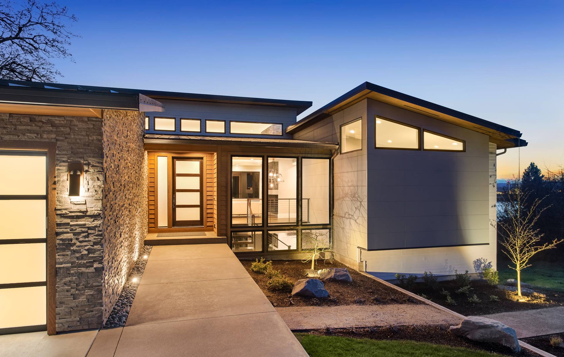 Modern luxury home exterior at sunset with glowing interior lights