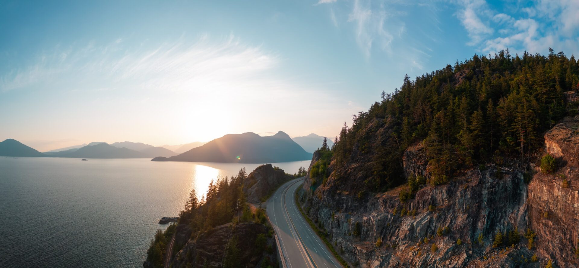 Coastal highway winding along forested cliffs above the ocean at sunset